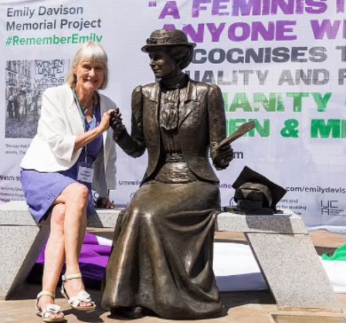 Sculptor Christine Charlesworth next to bronze statue of Emily Wilding Davison sitting on a bench