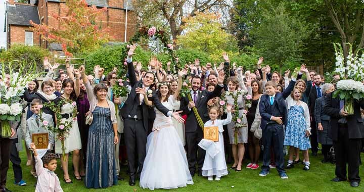 weddings guests with bride and groom holding hands in the air and smiling at camera