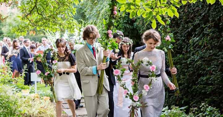 Bride and wedding guests parading through gardens with flowers and greenery