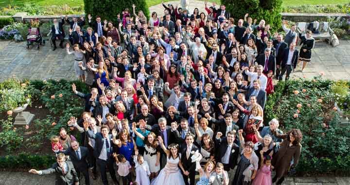 100 wedding guests with bride and groom taken from above whilst waving up at the camera outside on terrace