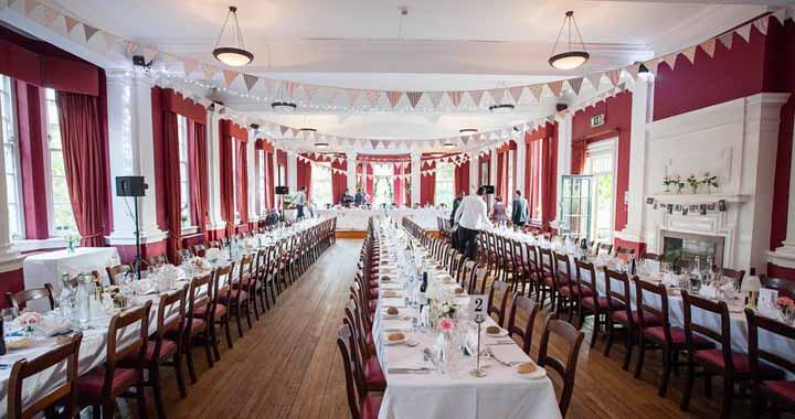 3 long banquet tables in dining hall set for wedding with flower decorations, bunting and tableware