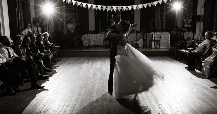 Black and white image of bride and groom dancing together in dining hall